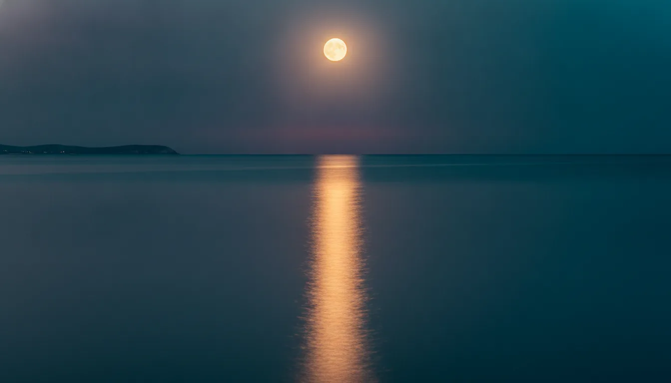 A full moon rising over a calm ocean at dusk with a path of light on the water